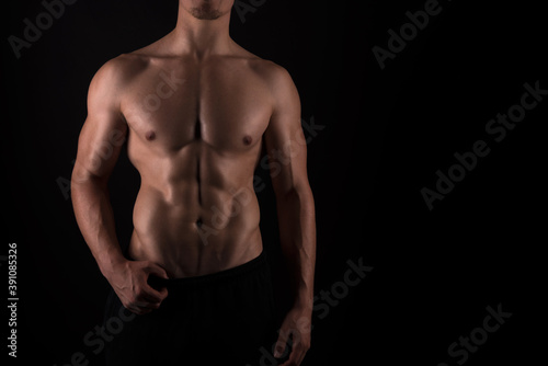 Muscular male torso of fit bodybuilder on black background
