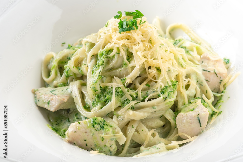Tagliatelle pasta with pesto, chicken and Parmesan in a white plate, close up
