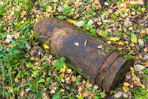 An old rusty military shell lies in the moss in the forest.