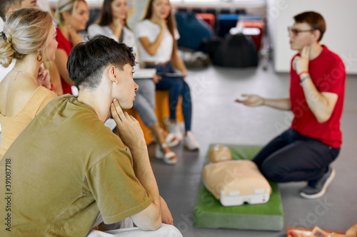 group of young caucasian people learning how to safe a life sitting together on lesson, discussing all techniques, using mannequin to show an example photo