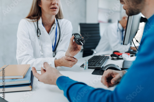 Female doctor measuring the blood sugar level of a young male patient with a glucometer. photo