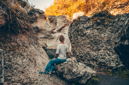 A woman travels through the mountains  sits on a stone and looks at the panorama. Hike to the mountain gorge. Active autumn rest