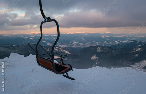 Alpine resortr ski lift with seats going over the sunset mountain skiing  slopes in extremally windy weather photo
