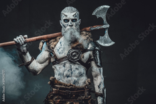 Risen from the dead northern warrior in smokey background with huge two handed axe on his shoulders staring at camera.