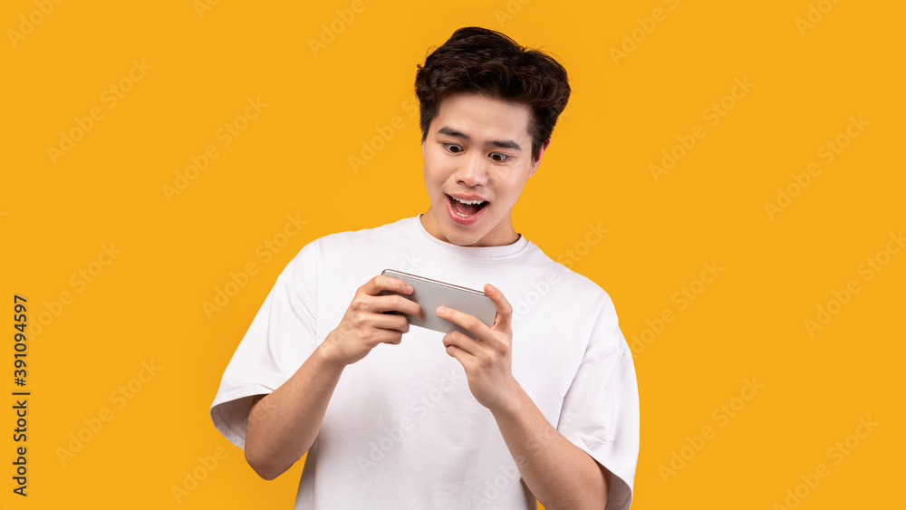 Excited asian man playing mobile games on orange background