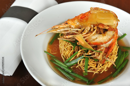 Yee Mee Fried Noodle with Big Prawn on top and some spring onion on top, served in a white plate.