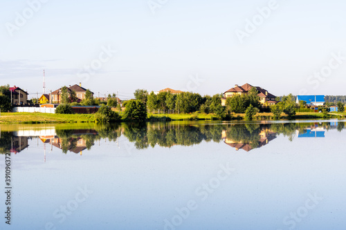 country houses on the lake behind the trees, the reflection of houses in the water.