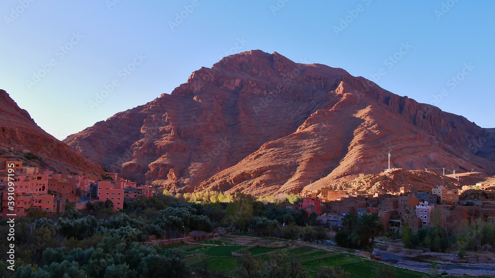Fototapeta premium Small Berber village near Tinghir, Morocco at the entrance of famous Todgha Gorges in the Altas Mountains with red colored rocks in the morning sun.