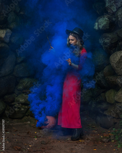 woman witch in red dress in a medieval castle with smoke blue pumpkin. The medieval queen. Evil witch