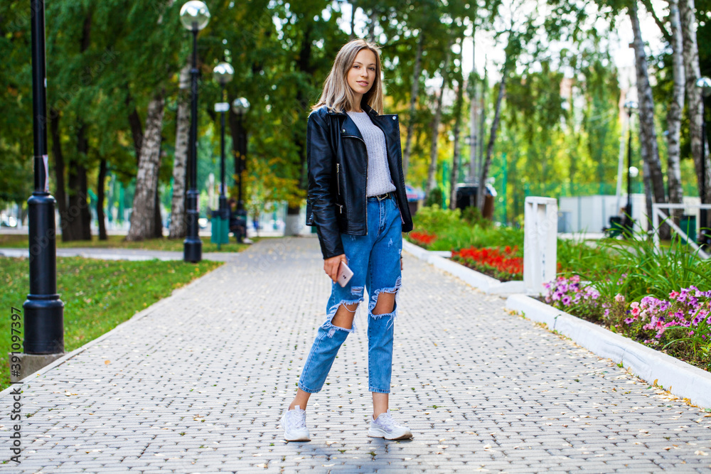 Young girl in a woolen sweater and torn jeans posing in an autumn park Young girl in a woolen sweater and torn jeans posing in an autumn park