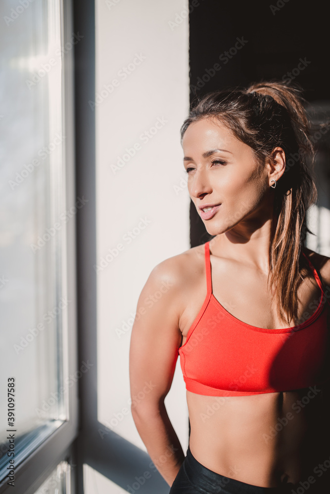 Slim athletic fit girl with pronounced abdominal muscles after workout by the window - workout satisfaction