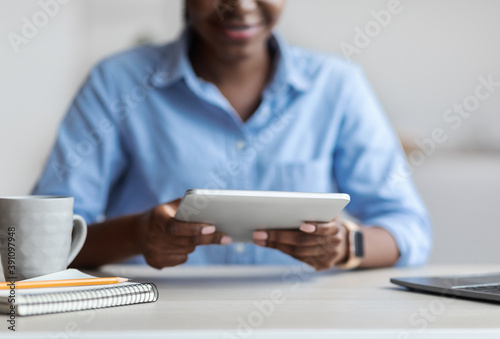Unrecognizable Black Female Using Digital Tablet While Sitting At Workplace In Office