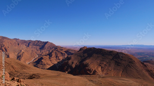 Fototapeta Naklejka Na Ścianę i Meble -  Beautiful panoramic view of the southern foothills of the Atlas Mountains near Tinghir, Morocco with the entrance to famous Todgha Gorges and red colored rocks on a cold winter day with blue sky.