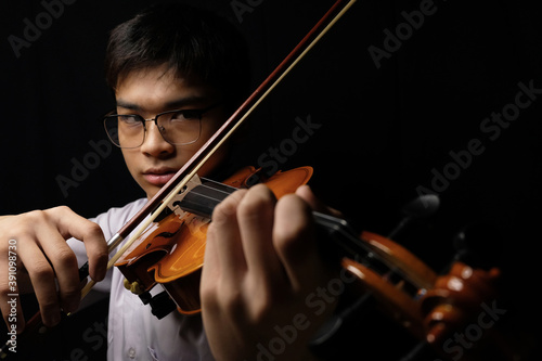 Young Asian man playing violin on dark background