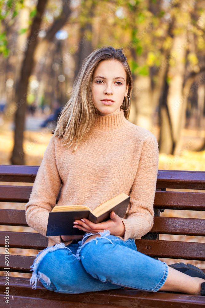 Beautiful blonde girl with a book sits on a bench in an autumn park Beautiful blonde girl with a book sits on a bench in an autumn park