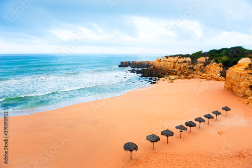Beautiful beach with yellow sand and umbrellas in Algarve, Portugal. Shore of Atlantic ocean. Beautiful summer seascape, famous travel destination