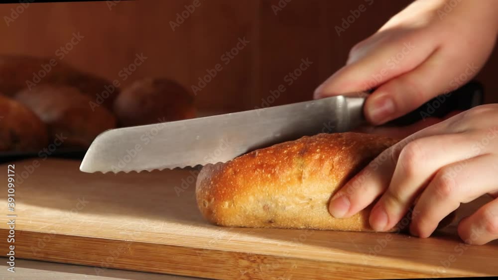 Female hands slicing with a knife crusty bread with olives on wooden table in the kitchen on a sunny day Female hands slicing with a knife crusty bread with olives on wooden table in the kitchen on a sunny day