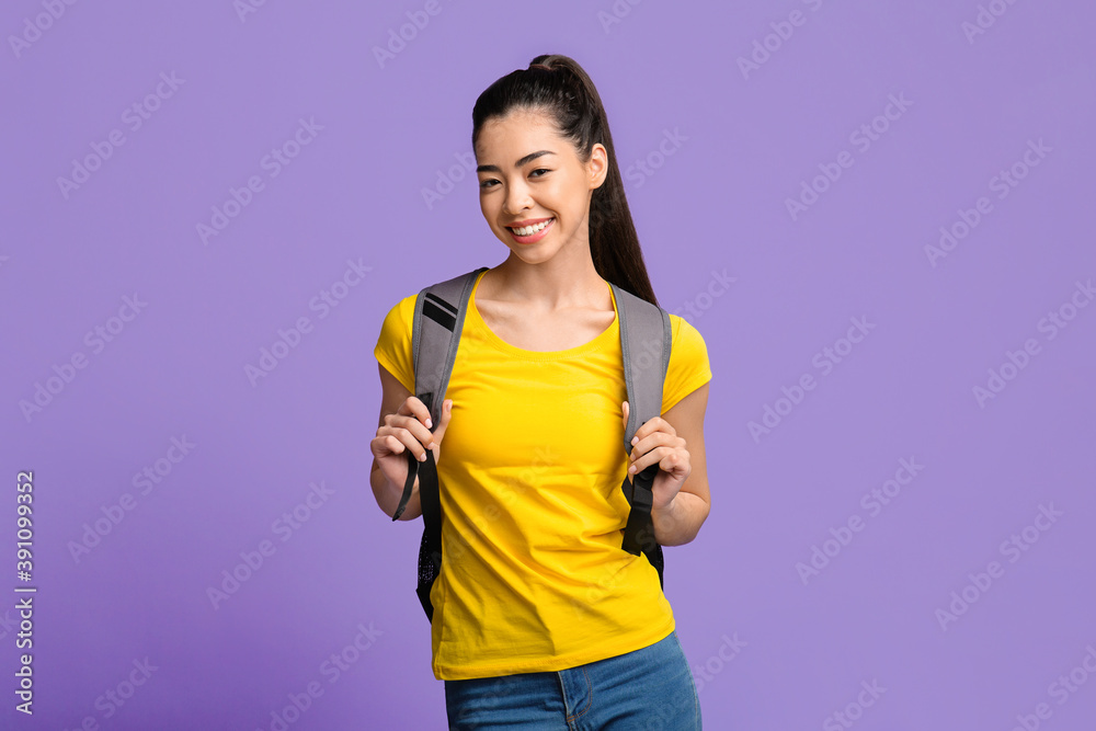 Young Beautiful Asian Female Student With Backpack Posing Over Purple Studio Background Young Beautiful Asian Female Student With Backpack Posing Over Purple Studio Background