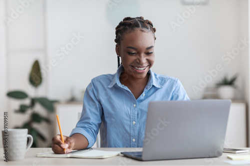 Online Education. Young Black Female Student Using Laptop At Home, Taking Notes