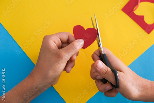 Paper crafts for kids. Child hands cutting colored paper with scissors at the table. Top view photo