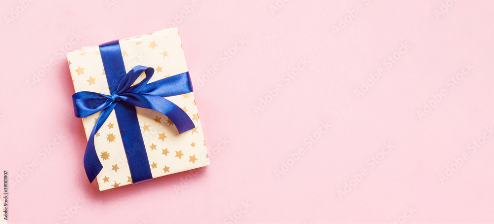 wrapped Christmas or other holiday handmade present in paper with blue ribbon on pink background. Present box, decoration of gift on colored table, top view with copy space wrapped Christmas or other holiday handmade present in paper with blue ribbon on pink background. Present box, decoration of gift on colored table, top view with copy space