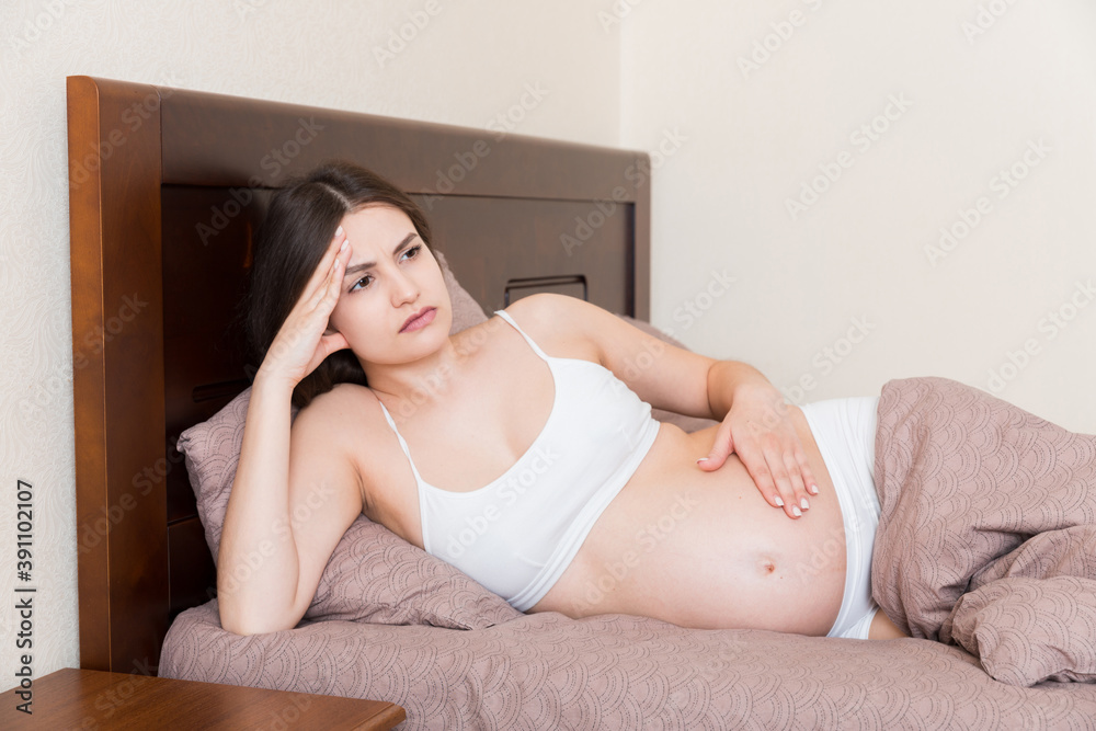 Young pretty pregnant woman suffering from headache at home in bed Young pretty pregnant woman suffering from headache at home in bed