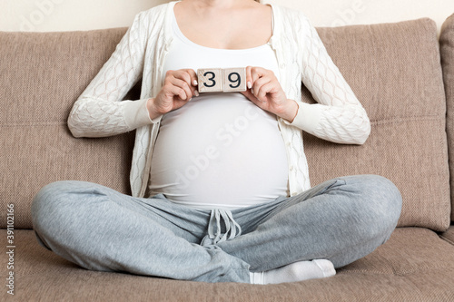 Pregnant woman in white underwear on bed in home holding calendar with weeks 39 of pregnant. Maternity concept. Expecting an upcoming baby