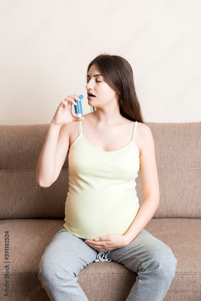 pregnant woman using asthma inhaler during attack for being healthy on sofa at the home. Healthy millennial Health care concept pregnant woman using asthma inhaler during attack for being healthy on sofa at the home. Healthy millennial Health care concept
