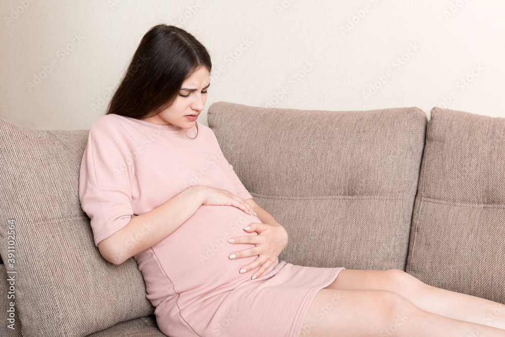 Pregnant Lady Having Massaging Lower belly Sitting On Sofa Indoor. Pregnancy Problems Concept. Maternity healthcare Pregnant Lady Having Massaging Lower belly Sitting On Sofa Indoor. Pregnancy Problems Concept. Maternity healthcare