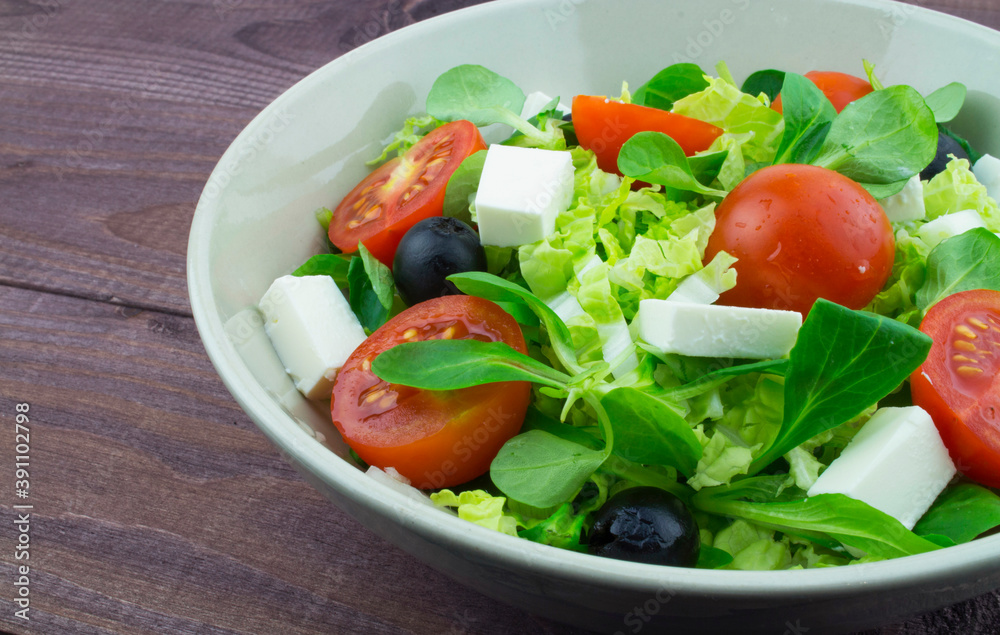 Salad in a white plate, fresh tomatoes olives feta cheese lettuce. A simple Greek salad recipe based on fresh vegetables and farm cheese