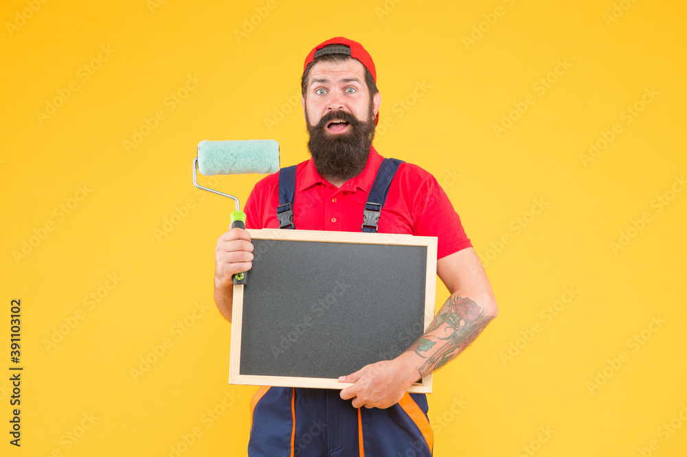 surprised bearded male painter worker in boiler suit uniform using paint roller tool for painting wall and hold blackboard for copy space advertising, skilled master wanted surprised bearded male painter worker in boiler suit uniform using paint roller tool for painting wall and hold blackboard for copy space advertising, skilled master wanted