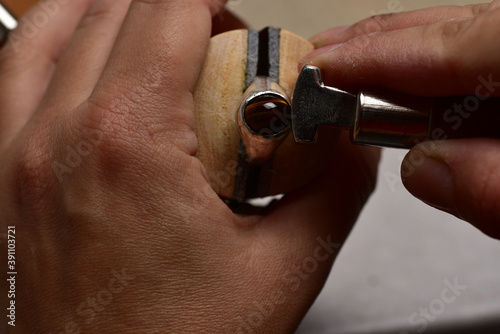 Jeweler making bezel setting for the silver ring with a cabochon tiger eye stone photo