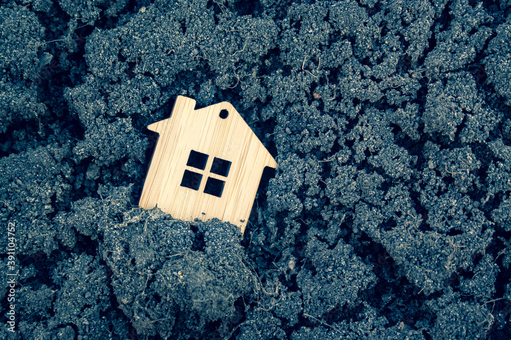Naklejka premium Miniature wooden toy house standing in the cracked black ground close up. Mortgage, rent, realtor, real estate concept