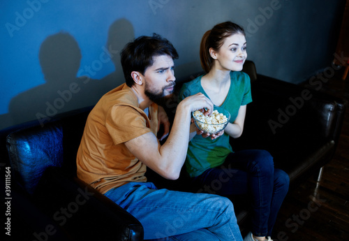 Friends man and woman watching TV on the couch and popcorn in a plate