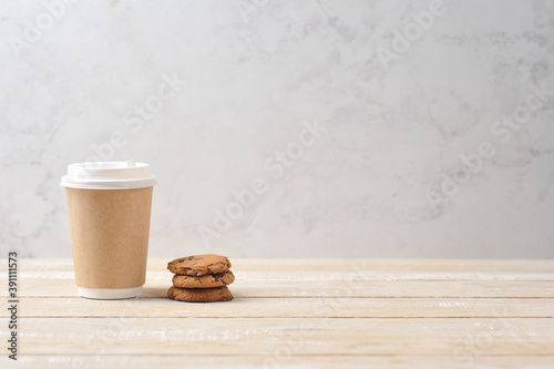 Paper glass with a hot drink on a light wooden background.  Oatmeal cookies with chocolate chips next to a glass.  The concept of a quick and tasty snack.