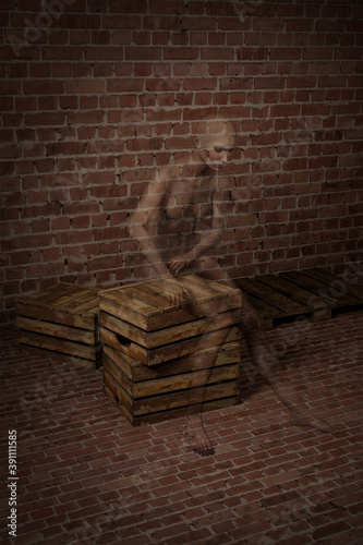 Young woman sits huddled on a stack of wooden pallets and fuses with the texture of a brick wall
