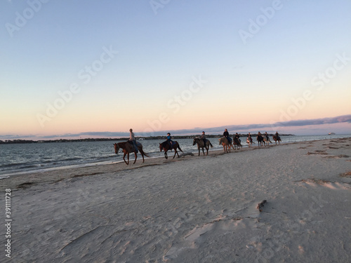 people on horseback on the beach at sunset