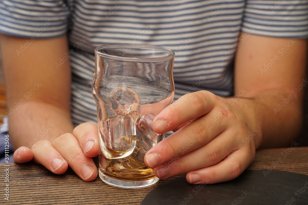 An autistic teenager sitting on a terrace. He has a glass with ice cubes and the rests fo soft drink in it. His hands show small wounds of picking on his skin or mild self mutilation. An autistic teenager sitting on a terrace. He has a glass with ice cubes and the rests fo soft drink in it. His hands show small wounds of picking on his skin or mild self mutilation.