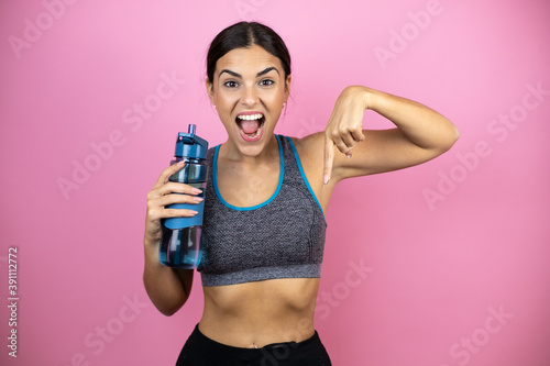 Young beautiful woman wearing sportswear over isolated pink background pointing finger down surprised.