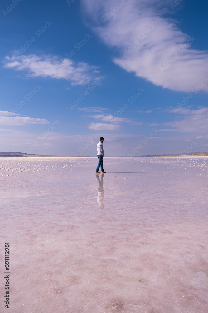 man walking on the salt lake with blue sky background. his reflection on shallow water. the concept of peace, quiet, loneliness and rest.