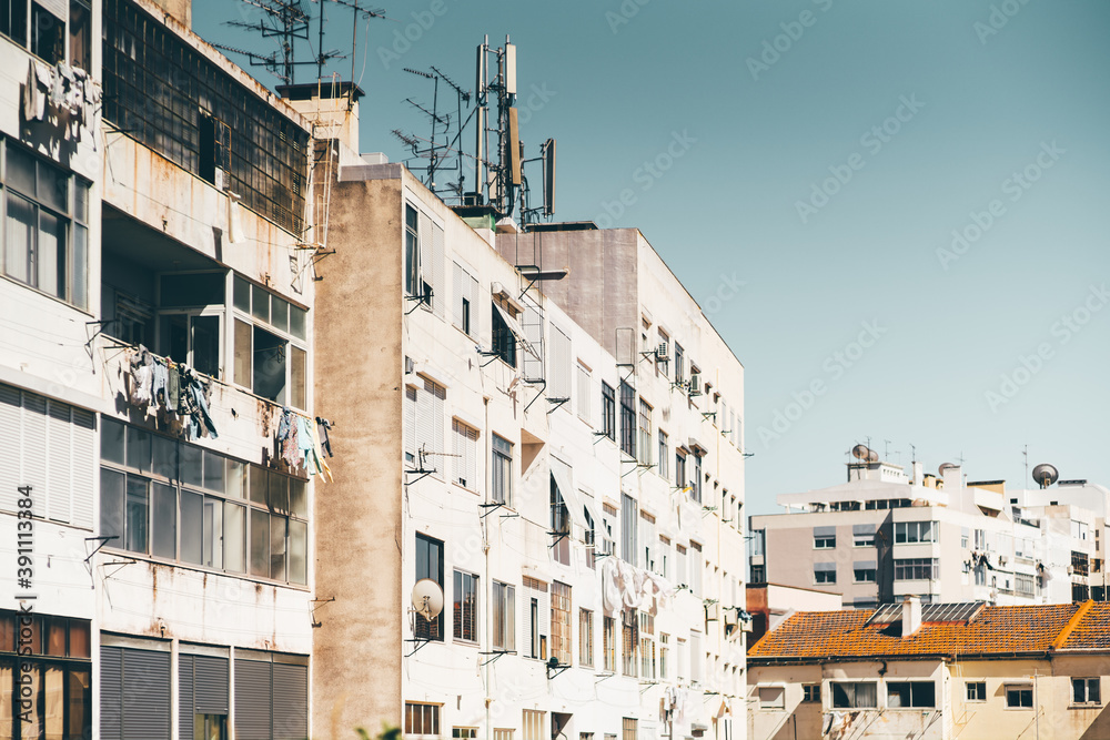 Multiple dwelling houses in a typical residential district of a europian uptown with buildings facades, balconies, dirt and rust, windows, drying laundry, roofs; a very sunny day, Lisbon, Portugal