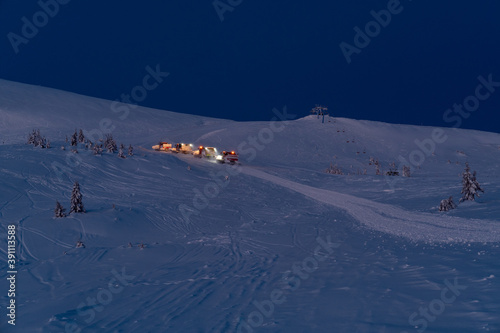 Snow groomers (snowcat ratrack machines) on night predawn excursion ride to winter mountain top with freeriders snowboarders. Dragobrat, Ukraine. People, mashine models and signs unrecognizable. photo