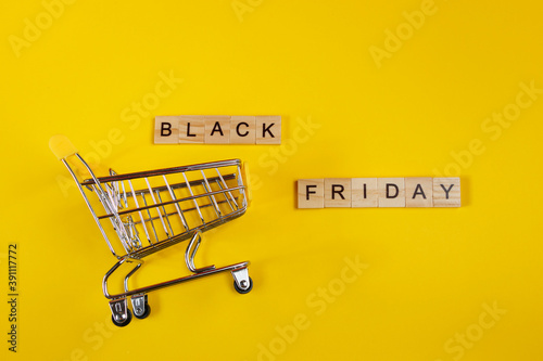 Sale and Black Friday concept. Mini shopping cart on yellow background.