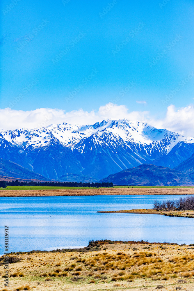 Snow covered mountains and green valleys with a lake in New Zealand