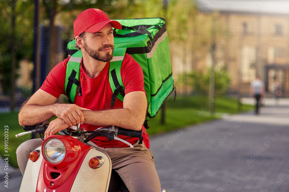 Young caucasian delivery man on scooter looking aside