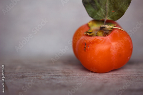 Orange ripe persimmon with dried leaf on grey wooden background, close up