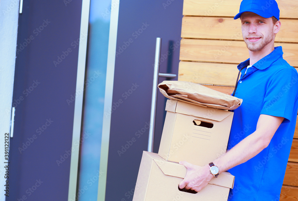 Smiling delivery man in blue uniform delivering parcel box to recipient - courier service concept. Smiling delivery man in blue uniform Smiling delivery man in blue uniform delivering parcel box to recipient - courier service concept. Smiling delivery man in blue uniform