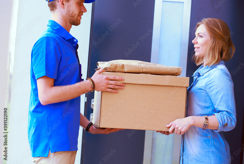 Smiling delivery man in blue uniform delivering parcel box to recipient - courier service concept. Smiling delivery man in blue uniform Smiling delivery man in blue uniform delivering parcel box to recipient - courier service concept. Smiling delivery man in blue uniform
