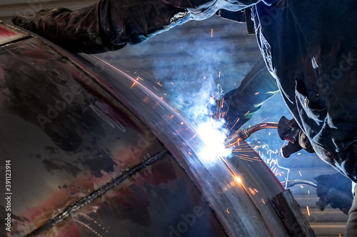 The welder is welding to steel material with gas metal arc welding proces. It sometimes referred to by its subtypes metal inert gas (MIG) welding or metal active gas (MAG) welding.