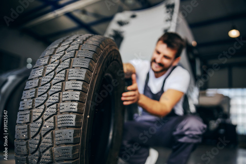Hardworking experienced worker holding tire and he wants to change it. In background is truck. Selective focus on tire. photo